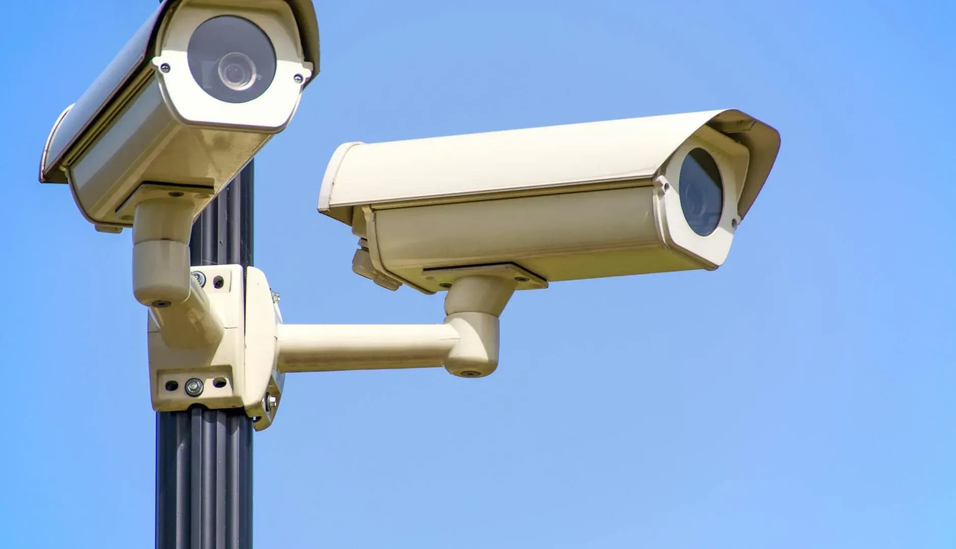 Outdoor security cameras mounted on a pole against a clear blue sky, providing surveillance for website maintenance security.