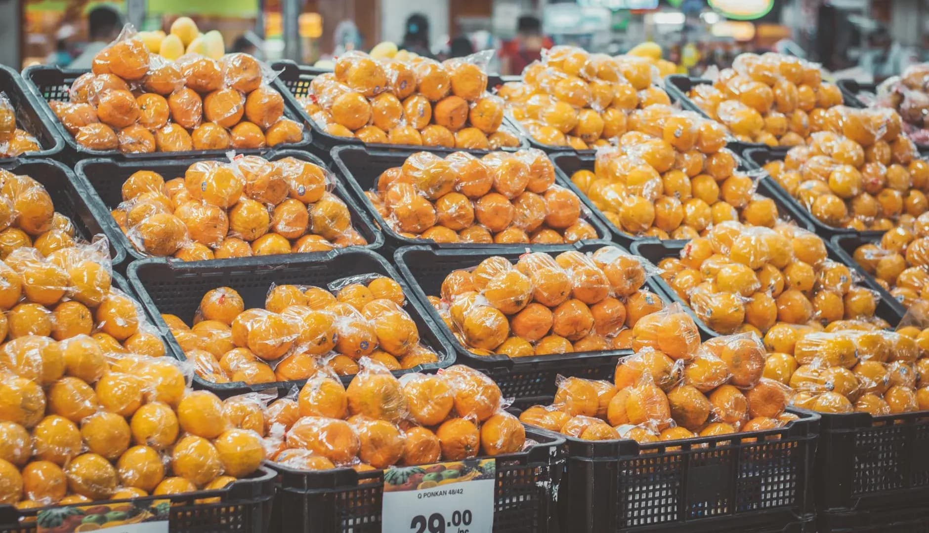 Stack of fresh oranges in plastic wrap with price tags displayed in a grocery store.
