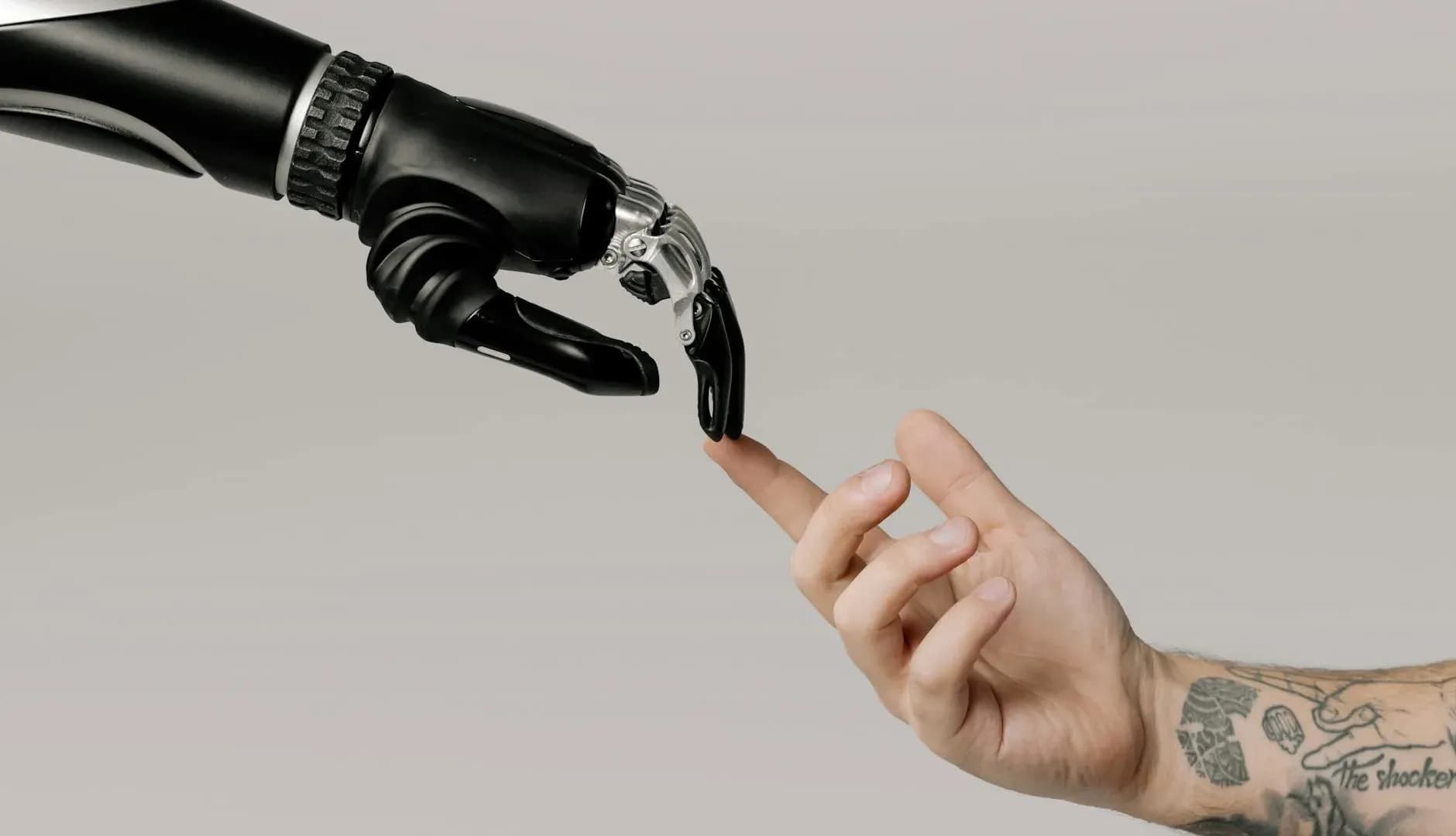 A tattooed human hand reaching out to a robotic hand on a white background, symbolizing AI technology collaboration.